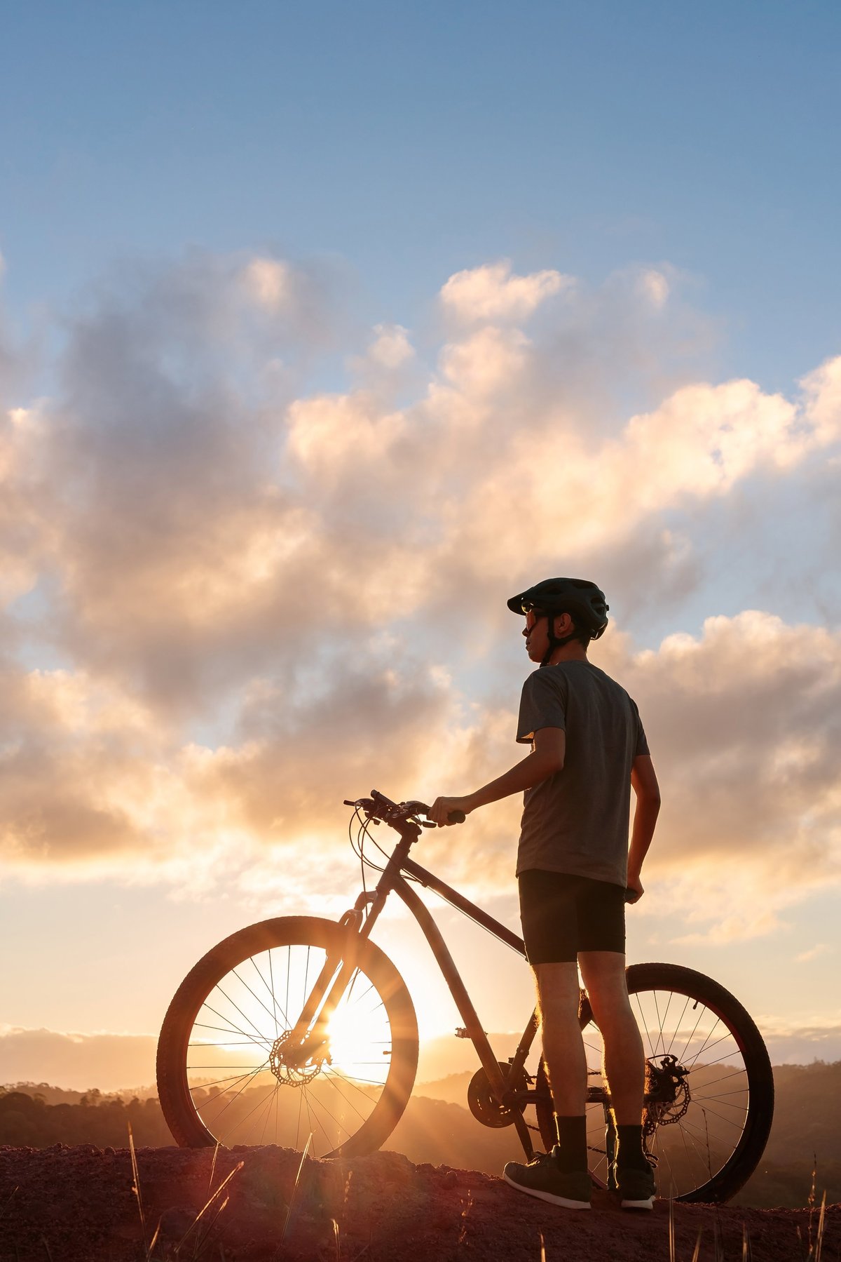 Cyclist standing with bike at sunset on mountain trail