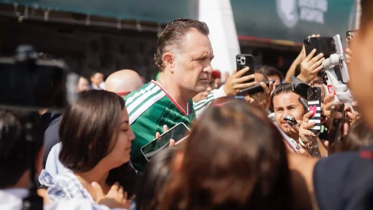 A man in a green and white scarf signs autographs for fans during a public appearance
