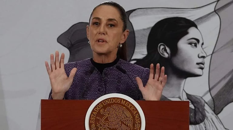 Woman in purple jacket speaking at podium with Mexican seal, gesturing with raised hands during speech
