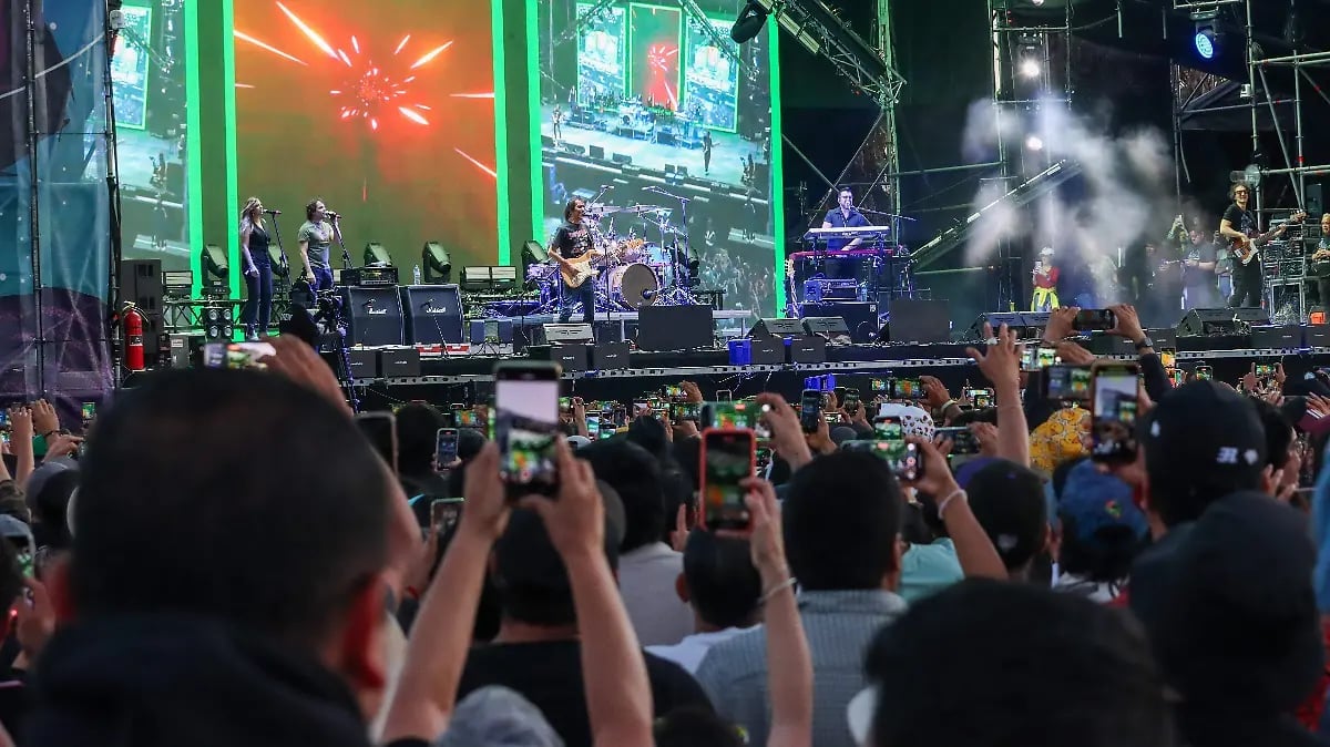 Large outdoor concert crowd with audience members holding up phones to record the stage performance with live band and green lighting