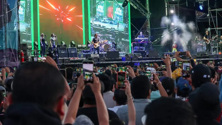 Large outdoor concert crowd with audience members holding up phones to record the stage performance with live band and green lighting