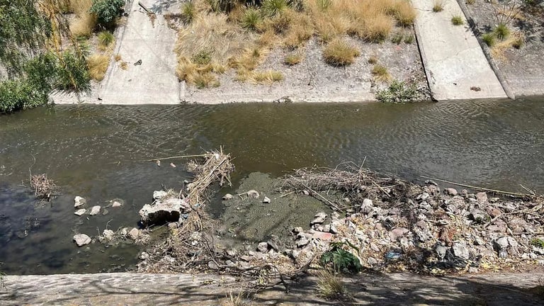 Aerial view of a river with concrete banks, rocky debris along the shore, and sparse vegetation on the embankment