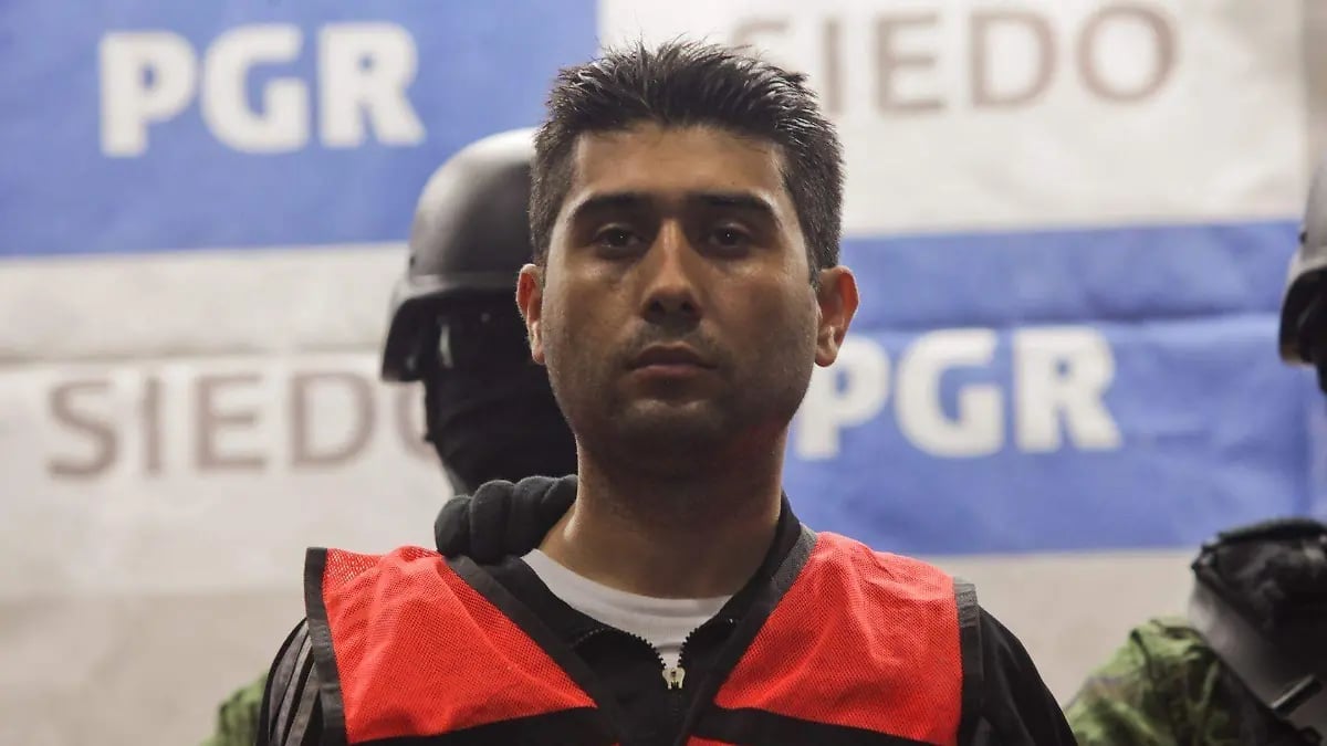 Man in red and black vest at press conference in front of PGR and SIEDO logos