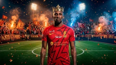 Football player wearing red jersey and crown standing on stadium field with cheering crowd, fire effects, and floodlights in background