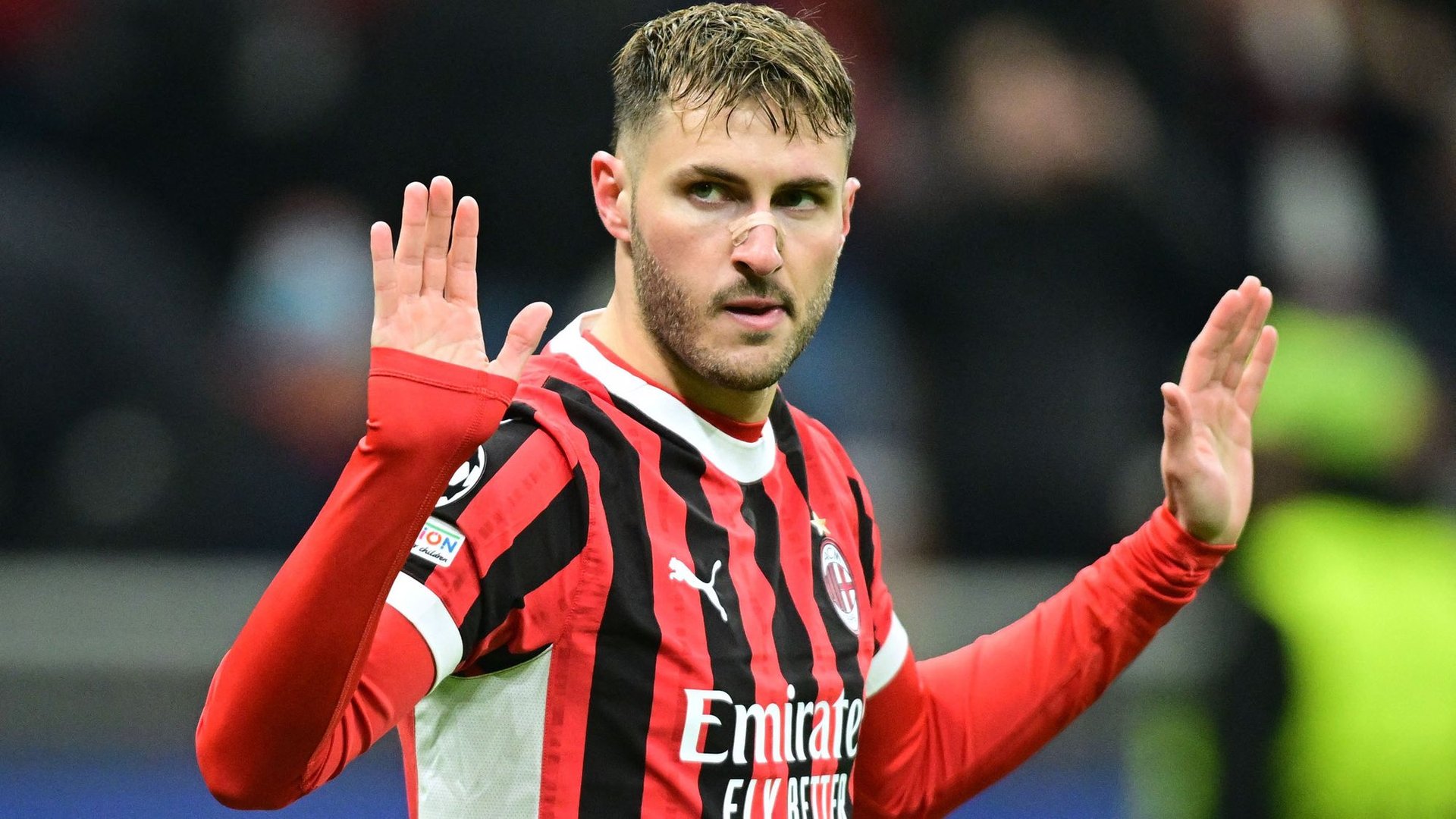 Football player in red and black striped AC Milan jersey with hands raised during a match
