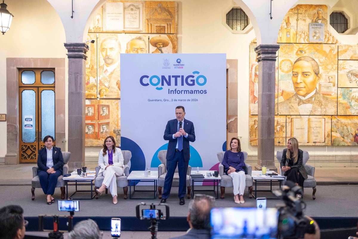 Business panel discussion with five speakers on stage behind a blue Contigo Informamos banner in an ornate hall