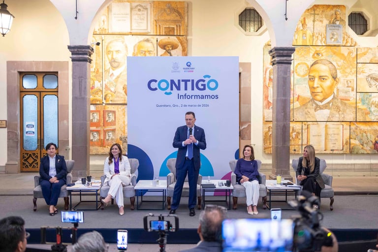 Business panel discussion with five speakers on stage behind a blue Contigo Informamos banner in an ornate hall